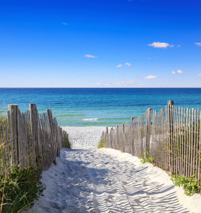 A beach with sand and fence leading to the ocean.